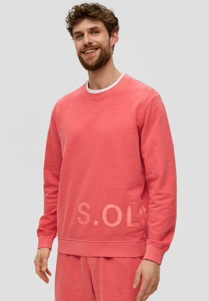 Sweatshirt corail avec col ras du cou, poignets et ourlet côtelés. Présente un logo discret à l'avant. Fabriqué en tissu doux et texturé.
