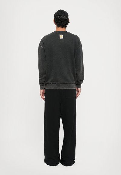 Grauer, übergroßer Sweatshirt mit gerippten Bündchen und Saum, ausgestattet mit einem quadratischen Etikett am Hals, kombiniert mit weiten schwarzen Hosen.
