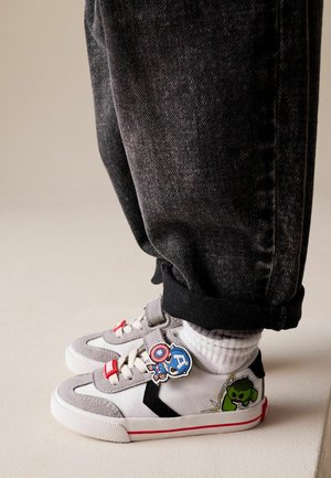 Gray sneakers with white soles feature comic character patches, a red accent strap, and black detailing. Worn with rolled black jeans.