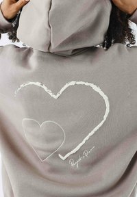 Sudadera gris con un gran diseño de corazón texturizado en blanco en la parte posterior, con texto bordado debajo. Fabricada en un tejido suave y con un corte relajado.