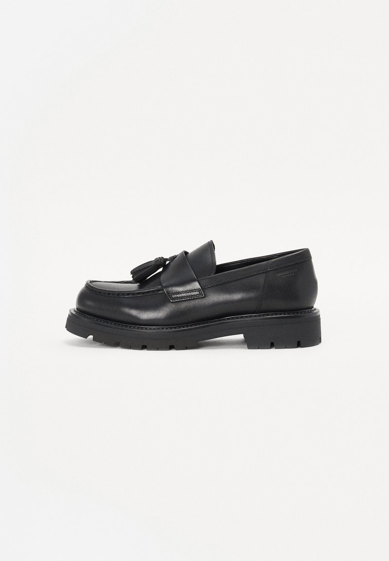 Mocasines de cuero negro con detalles de borlas, punta cuadrada y suela de goma gruesa. Textura suave con costuras tonales y acentos mínimos.