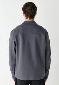 Grau gestreiftes Hemd mit Kragen, langen Ärmeln und Rückenpasse. Es hat einen geraden Saum und Knopfdetails an den Manschetten.