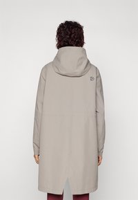 Beige hettejakke med lange ermer, høy-lav kant og logodetalj nær hetten. Glatt tekstur og minimalistisk design.