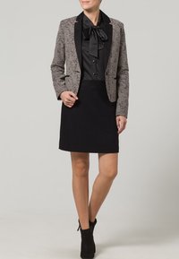 Grå mönstrad blazer med svarta slag, tillsammans med en svart blus med en stor båge och en svart kjol. Bärs med ankelstövlar.