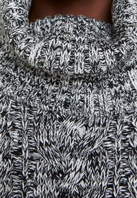 Schwarz-weißer Strickpullover mit Rollkragen, der ein strukturiertes Muster und einen ausgeprägten, gerollten Kragen aufweist. Nahaufnahme des Stoffdetails.