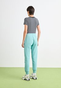 Mintgrønne joggebukser med elastisk midje og mansjetter, sammen med en svart og hvit stripete t-skjorte, iført hvite og svarte sneakers.
