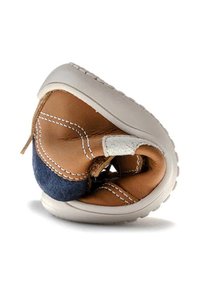 Zapato para bebé de cuero marrón y denim con una suela de goma blanca flexible, que incluye costuras blancas y un diseño plegable.