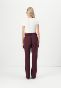 Pantalons bordeaux à jambes larges avec une taille élastique, associés à un haut ajusté à manches courtes blanc. Texture de tissu lisse.