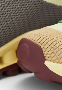Sportska obuća s pletenim sivo-gornjim dijelom, bež prednjim dijelom s teksturiranim detaljima i bordo gumenim potplatom s kružnim detaljem.