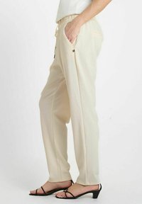 Beige broek met een ontspannen pasvorm, elastische tailleband, trekkoord en zijzakken. Gemaakt van zachte stof met een gladde textuur.