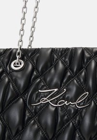 Bolso de mano de piel acolchada negra con una correa de cadena de metal plateado y un destacado acento de logo plateado. Superficie texturizada con patrones en forma de diamante.
