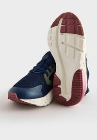Baskets de sport en maille marine avec des accents gris, un bout texturé et une semelle blanche mouchetée avec un talon en caoutchouc rouge et un motif de semelle.