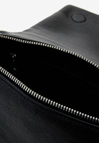 Una pochette nera in pelle con chiusura a zip, caratterizzata da una superficie liscia e un interno scuro, che mostra cuciture ordinate e dettagli in metallo.