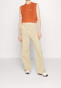 Orange sleeveless knit sweater with cable pattern, paired with light beige wide-leg pants. Additional details include black and pink sneakers.