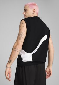 Maglione senza maniche nero con un grande design astratto bianco sulla schiena. Realizzato in tessuto a maglia, dotato di bordi a costine e vestibilità rilassata.