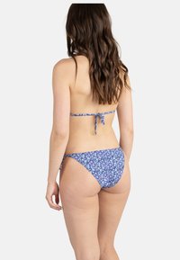 Bikini floral violet avec des accents blancs et bleus ; attaches réglables dans le dos et sur les côtés ; tissu lisse et léger ; coupe taille basse.