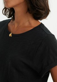 T-shirt noir à manches courtes avec un col rond décontracté et des manches retroussées, présentant une texture subtile et associé à un collier en or.