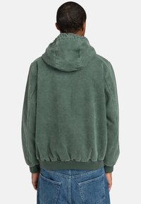 Sudadera verde con capucha de ajuste relajado, textura suave, dobladillo elástico y puños acanalados. Los detalles de costura visibles realzan el diseño.