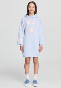 Jasnoniebieska sukienka z kapturem z napisem "VIRGINIA", długie rękawy i luźny krój. Posiada ściągacze przy mankietach i u dołu, zestawiona z niebieskimi sneakersami.
