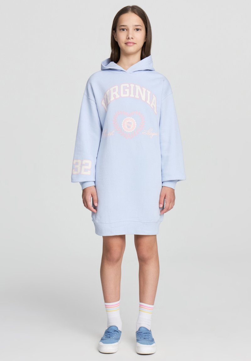 Jasnoniebieska sukienka z kapturem z napisem "VIRGINIA", długie rękawy i luźny krój. Posiada ściągacze przy mankietach i u dołu, zestawiona z niebieskimi sneakersami.
