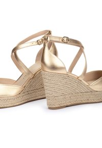Las sandalias de cuña metálica dorada cuentan con correas cruzadas en el tobillo y un tacón envuelto en yute texturizado. El forro interior suave complementa el diseño.
