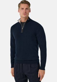 Pull en navy à zip quart en tissu doux et texturé, avec un col intérieur crème et des poignets et un ourlet côtelés. Doté d'un zip argenté avec une tirette en cuir.