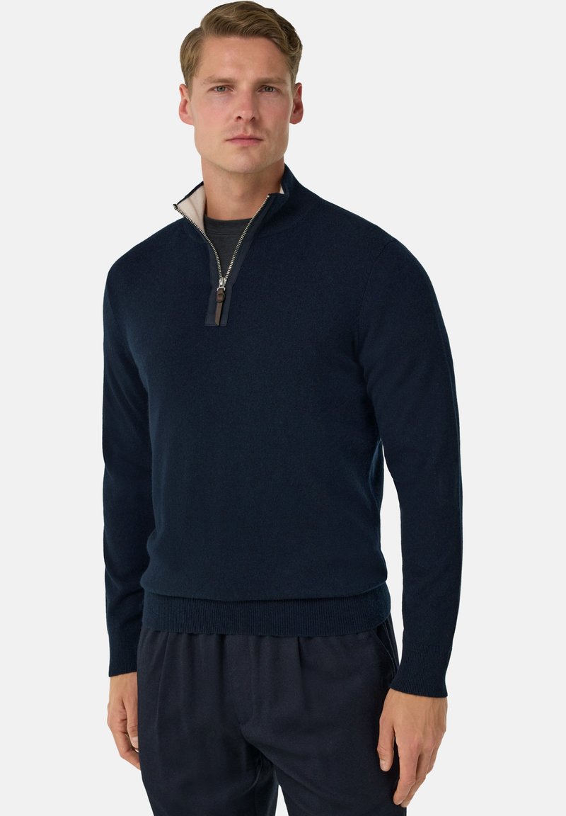 Pull en navy à zip quart en tissu doux et texturé, avec un col intérieur crème et des poignets et un ourlet côtelés. Doté d'un zip argent é avec une tirette en cuir.