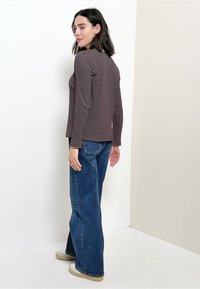 Gestreiftes langärmeliges Oberteil in Dunkelrot und Creme, kombiniert mit weit geschnittenen blauen Denim-Jeans. Die Schuhe haben eine cremefarbene Sohle. Einfache, lässige Stil.