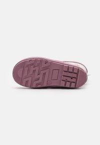 Semelle de sneaker en caoutchouc violet avec des motifs de texture, une semelle intermédiaire lisse et un détail de marque près du talon.