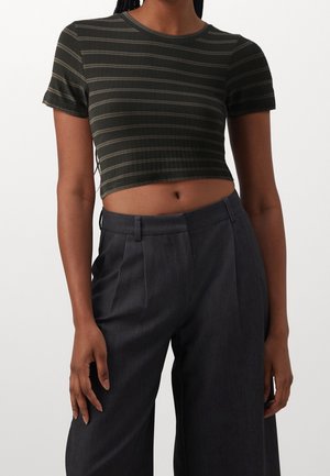 Frau trägt ein dunkelgrünes und graues gestreiftes kurz geschnittenes T-Shirt kombiniert mit hoch taillierten, dunkelgrauen, weit geschnittenen Hosen.