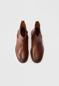 Bocanci ankle din piele maro cu o textură fină, având un fermoar pe fiecare جانبă și un design cu vârful rotunjit. Talpă subtil contrastantă.