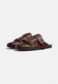 Smeđe kožne cipele na slip-on s detaljima od resica, srebrnom kopčom i ukrasnim perforacijama na prstima. Dizajn ravnog đona.
