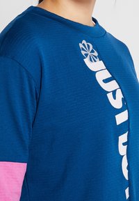 Blaues Kurzarm-T-Shirt aus strukturiertem Stoff, mit einem großen weißen Logo-Druck und pinken Akzenten an den Ärmeln.