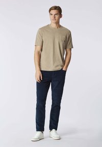 T-shirt beige in cotone con taschino sul petto, abbinata a pantaloni di velluto a coste blu navy e sneakers bianche. Design semplice e casual.