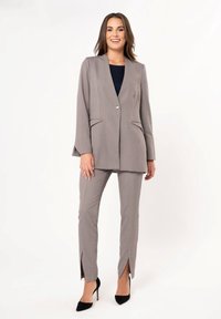 Gray tailored blazer with a single button, paired with gray pants featuring side slits. Material has a smooth texture; flared sleeves.