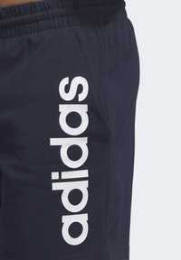 Mornarske sportske kratke hlače s mekim teksturom, s velikim bijelim "adidas" logotipom sa strane i elastičnom strukom za prilagodljivu lakoću nošenja.