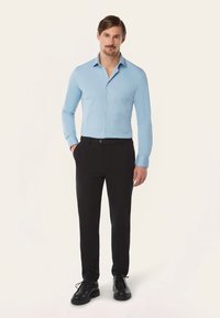 Lichtblauwe overhemd met lange mouwen, gecombineerd met zwarte broek en zwarte schoenen met een ronde neus en een stevige zool.