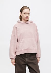 Rózsaszín kapucnis pulcsi kenguruzsebbel, húzózsinórral ellátott kapucnival és bordás mandzsettával. Puha anyag, apró logóval az elején.