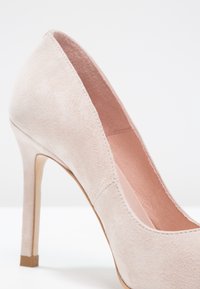 Escarpin à talon haut en daim beige avec bout fermé, design épuré, et doublure intérieure lisse, présenté de profil sur un fond blanc.
