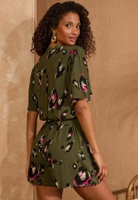 Zaļš īss romperis ar brīvu piegulumu, rotāts ar rozā un melnas krāsas ziedu rakstu. Mīksta tekstūra, īsas piedurknes un elastīga jostas detaļa.