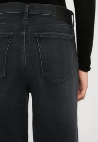 Fekete farmernadrág, szűkített derékbőséggel, közép magas üléssel és két hátsó zsebbel. Az anyag enyhén megkopott, sima tapintású.