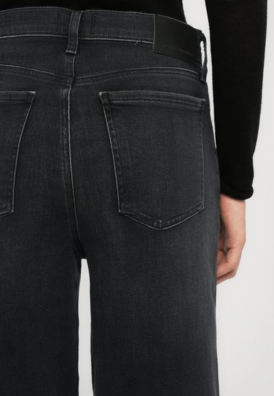 Jean en denim noir avec une taille ajustée, taille mi-haute et deux poches arrière. Le matériau est légèrement décoloré avec une texture lisse.