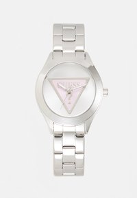 Montre en acier inoxydable argenté avec un cadran rond, présentant un triangle rose avec le logo "GUESS", et un bracelet poli de style maillon.
