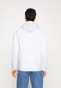 Sudadera blanca con capucha de textura suave, de mangas largas y con un bolsillo tipo canguro. Combinada con unos vaqueros azul denim de corte holgado.