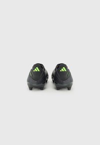 Black football boots with green accents, featuring a textured synthetic upper, low profile, and molded studs on the outsole for traction.