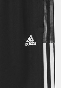 Pantalones deportivos negros con tres rayas verticales blancas a los lados, tela texturizada y un logo blanco de Adidas en la parte frontal.