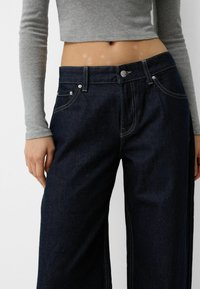 Dark blue wide-leg jeans made of denim, featuring contrasting yellow stitching, front pockets, and a metal button closure.