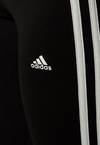Leggings atletici neri con design a tre strisce bianche e un piccolo logo Adidas bianco sulla coscia sinistra. Tessuto liscio e elasticizzato.
