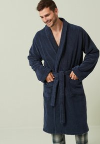 Tumši zils, frotē auduma apģērbs ar garām piedurknēm, jostu viduklī un divām priekšējām kabatām, ar šalli apkakli un mīkstu, tekstūru virsmu.