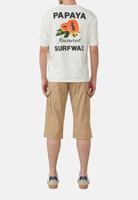 Weißes T-Shirt mit kurzen Ärmeln, auf dem "PAPAYA geschmackvolles SURFWAX" steht, und einer Papaya-Grafik, kombiniert mit beigen Cargo-Shorts und Sneakers.